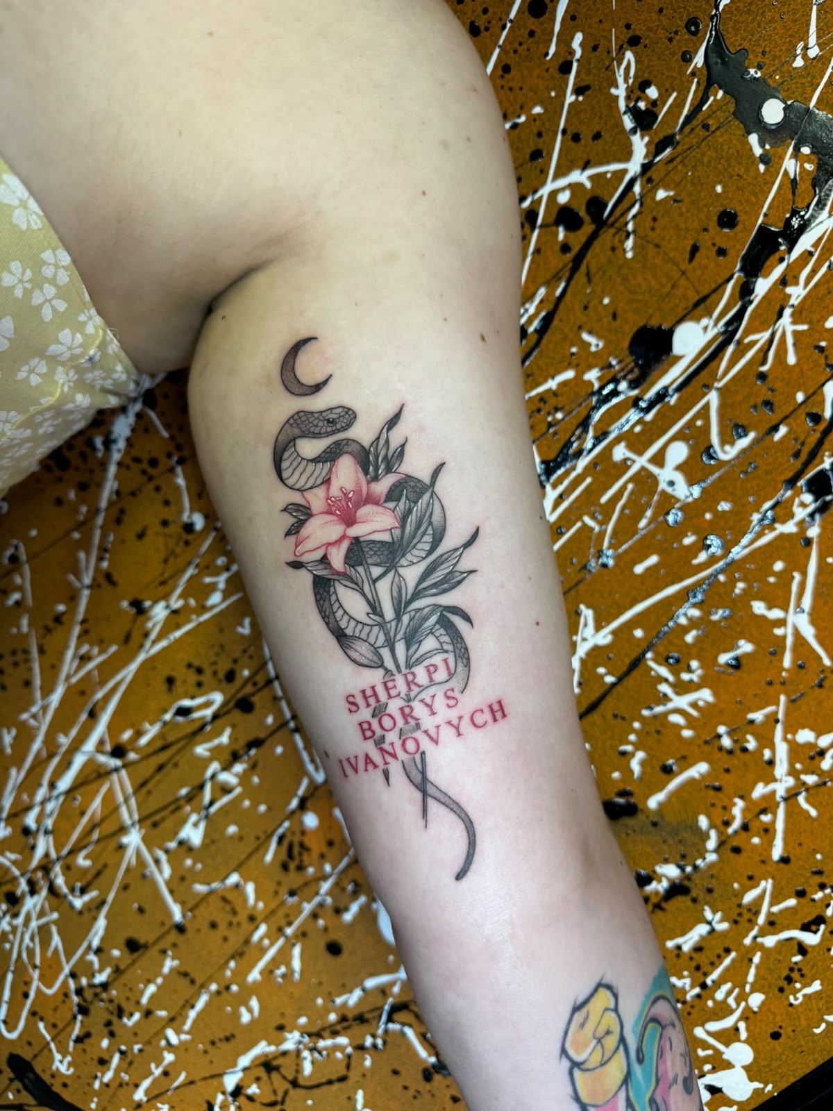 Ornamental snake, flower and lettering tattoo on the arm